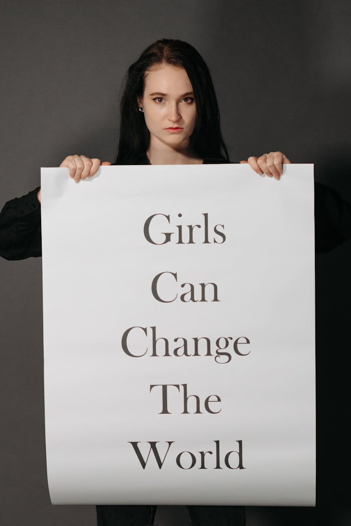 A woman holds a powerful sign stating 'Girls Can Change the World' on a gray background.